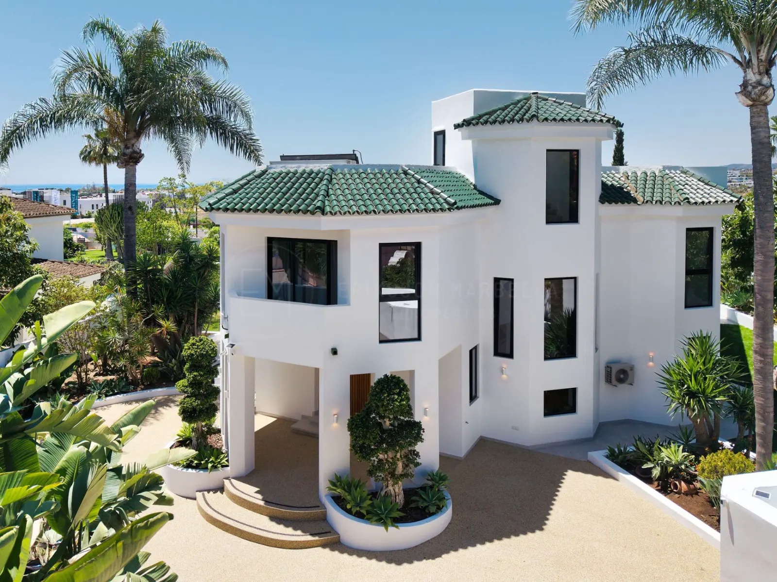 Aerial view of the finished villa with green tiled roofs, palms and sea beyond